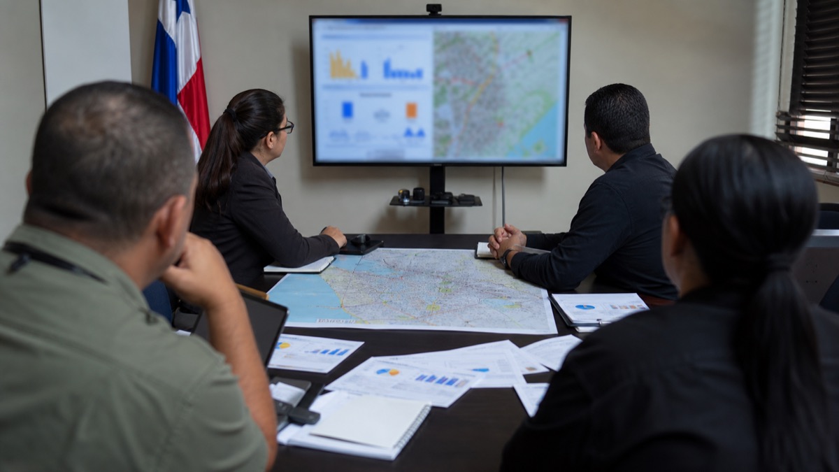 criminology and public-safety specialists in a neutral conference room reviewing a city map and anonymized charts in Panama, people shown from behind