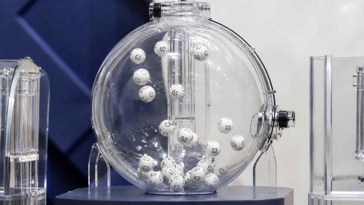 transparent lottery drum with numbered balls in a neutral studio, no readable text