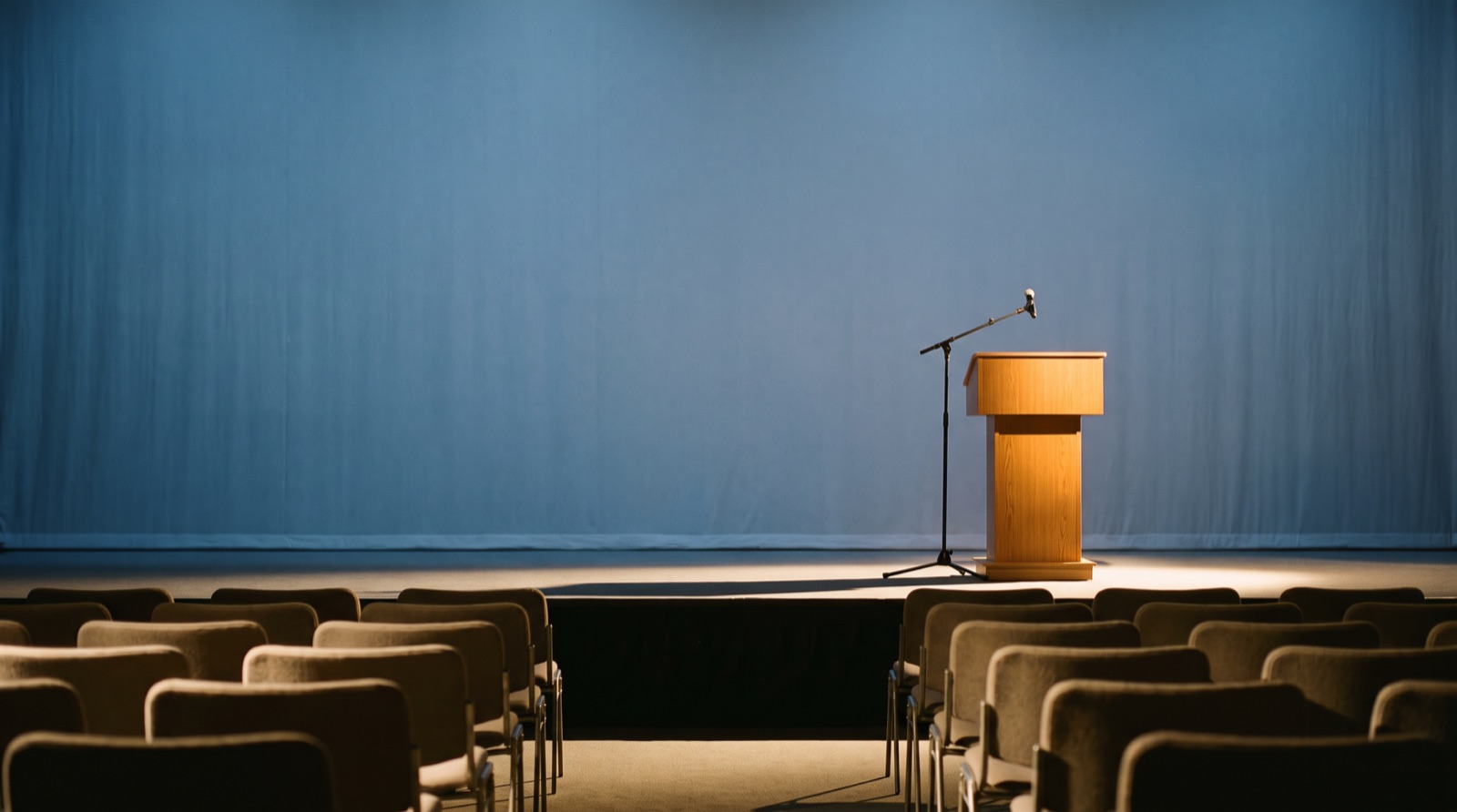 An empty conference stage with a lectern and seated rows before a policy presentation.