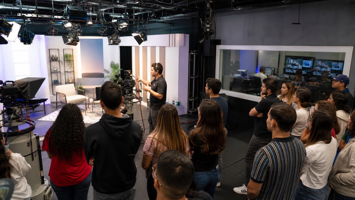 advertising students learning from media professionals inside a modern television production studio in Panama, cameras and control-room equipment visible, no identifiable personalities