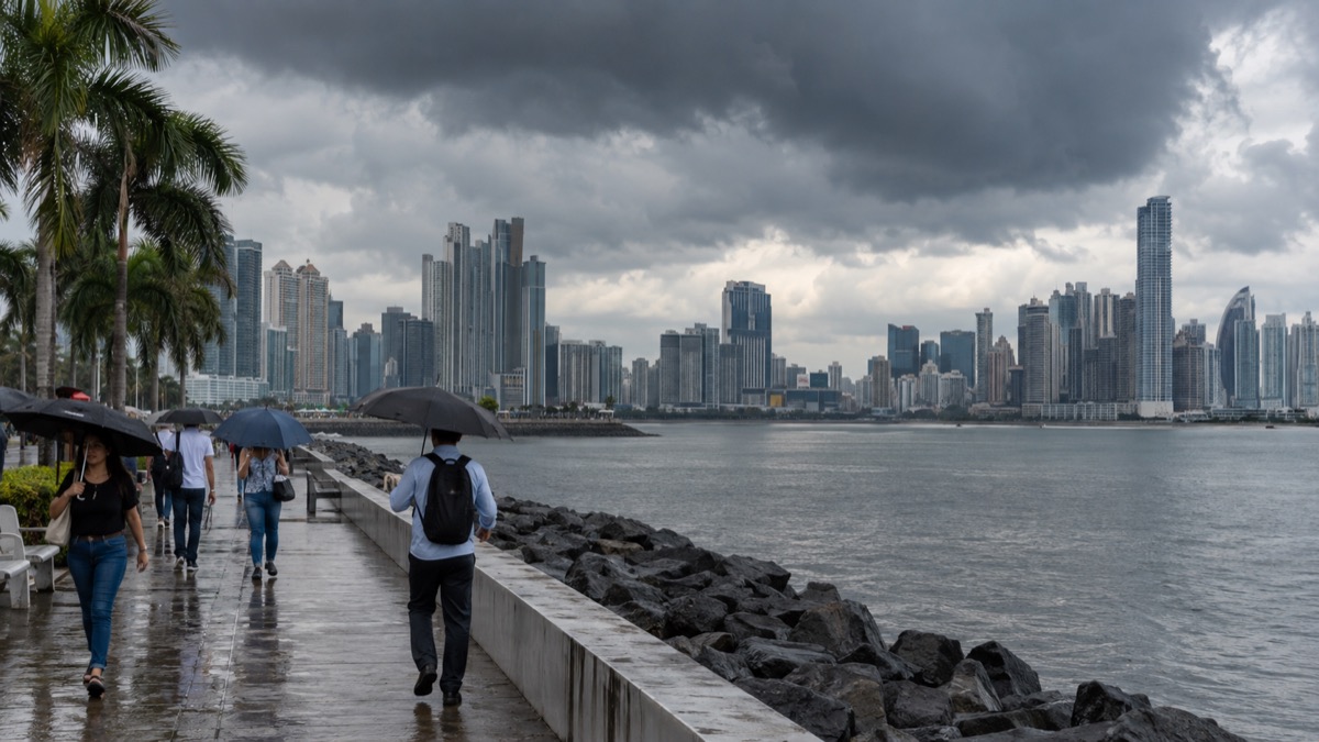 rain clouds gathering over Panama City skyline with residents carrying umbrellas, factual weather documentary scene