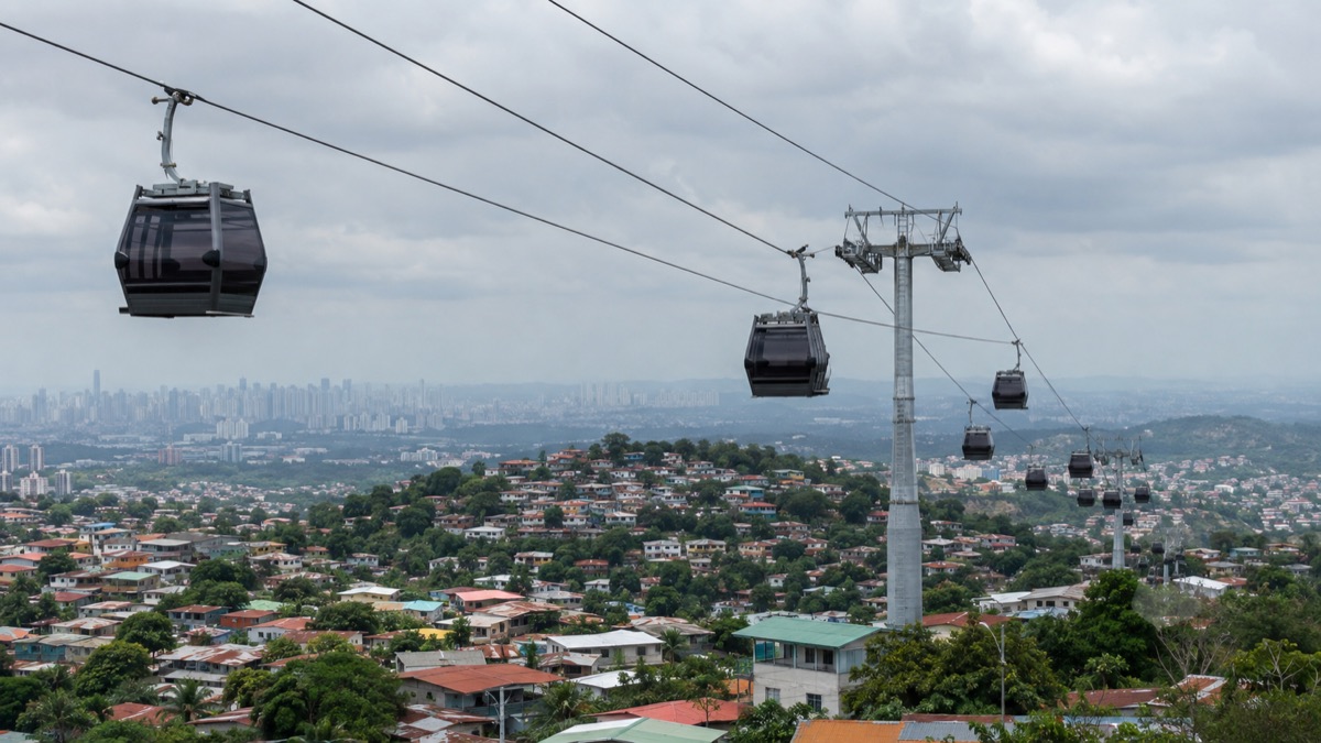 modern urban cable-car system above the hills and dense neighbourhoods of San Miguelito Panama, realistic infrastructure news photography, no branding