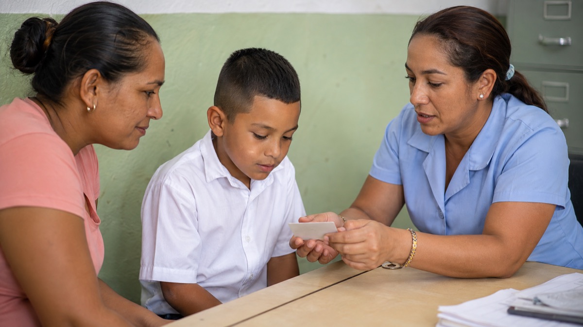 Panamanian parent and student reviewing education-support card information at a school service desk, card details hidden, warm documentary scene